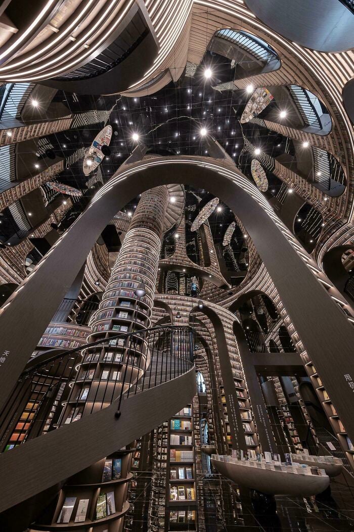 Grandiose library interior with towering bookshelves, spiral staircases, and reflective ceilings creating a magical atmosphere.