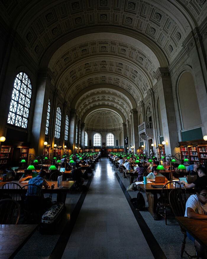 宏偉的圖書館內部，擁有高聳的拱形天花板、大型窗戶，以及一排排帶有綠色檯燈和讀者的書桌。