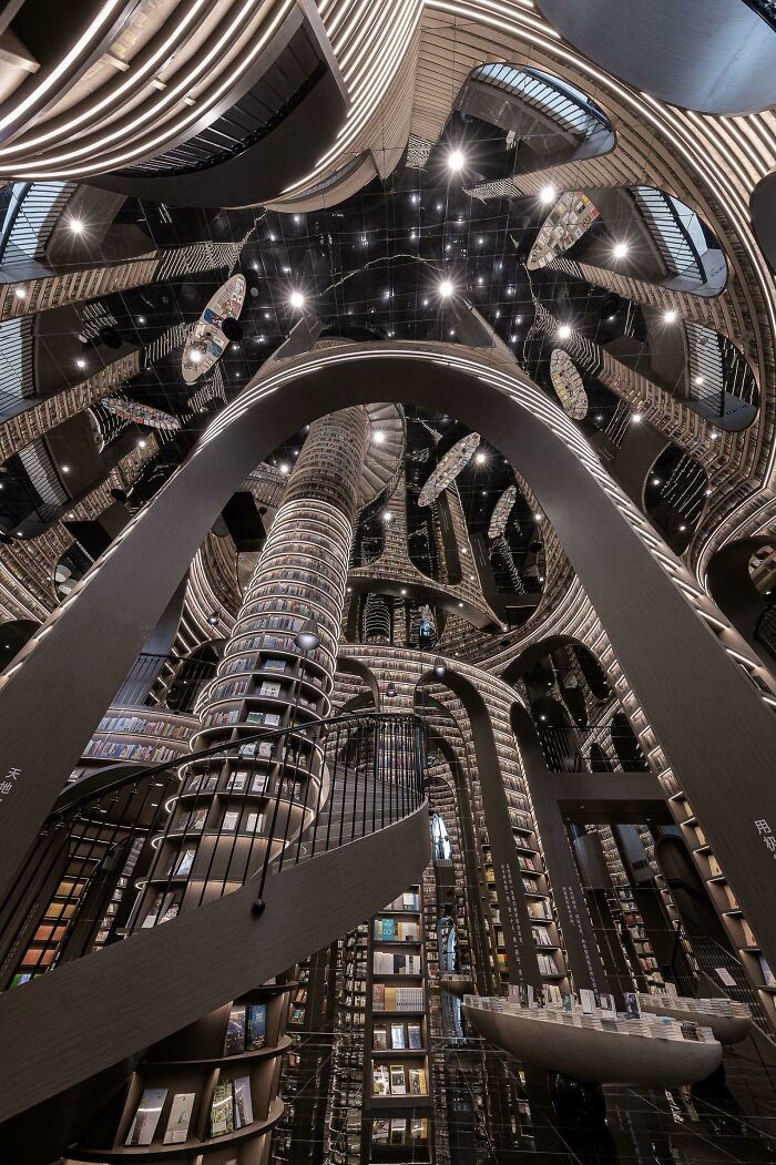 Grandiose library interior with towering bookshelves, spiral staircases, and reflective ceilings creating a magical atmosphere.