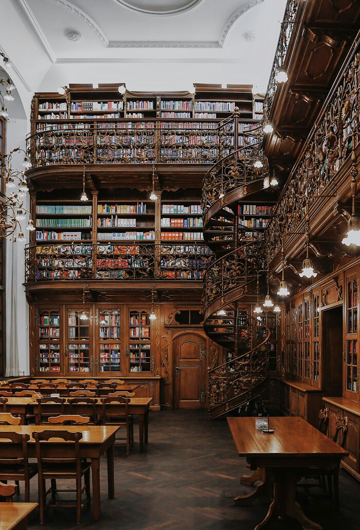 Grandiose library interior with wooden shelves, spiral staircase, and cozy reading tables filled with books worldwide.