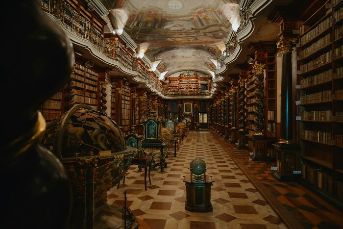 Grandiose library interior with antique globes, ornate columns, and rows of old books on wooden shelves.