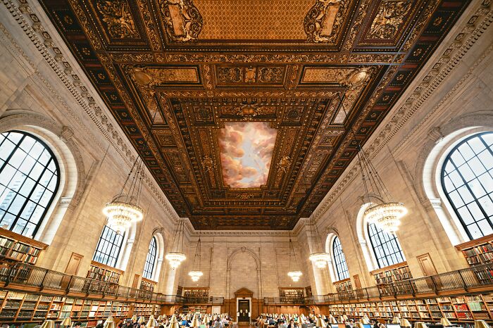 Grandiose library interior with ornate ceiling, large arched windows, chandeliers, and rows of bookshelves filled with books. Grandiose library interior with ornate ceiling, large arched windows, chandeliers, and rows of bookshelves filled with books.
