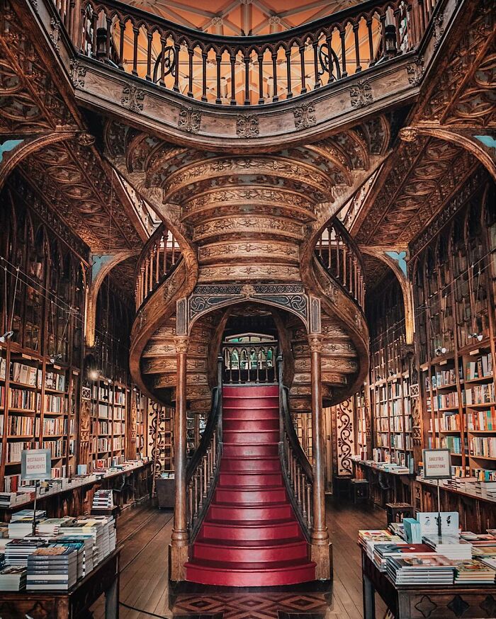 Ornate grandiose library with a carved wooden spiral staircase and rows of bookshelves filled with books around it.