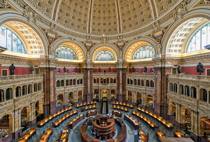 Grandiose and cosy library interior with ornate dome ceiling, arched windows, and rows of reading desks with warm lighting. Grandiose and cosy library interior with ornate dome ceiling, arched windows, and rows of reading desks with warm lighting.